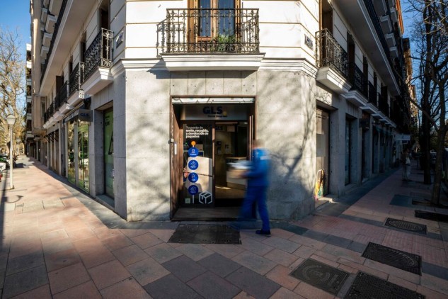 GLS Parcel Shop en esquina urbana, punto de recogida y envío de paquetes con persona entrando en la oficina