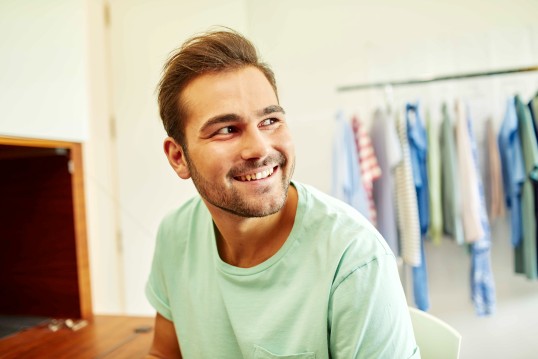young man smiling in front of a clothes rack