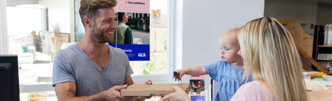 A woman with a phone in one hand and a parcel in the other entering a Parcel Shop