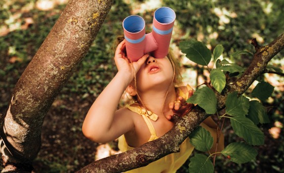 The little girl with binoculars is playing in the tree