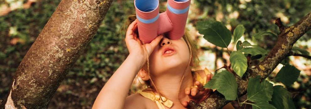The little girl with binoculars is playing in the tree