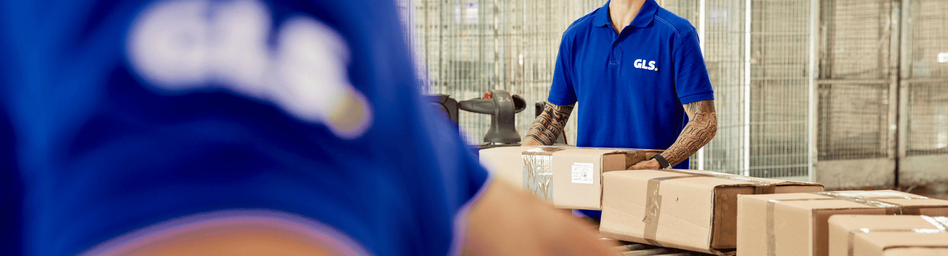 Two men in a depot moving boxes on a conveyor belt.